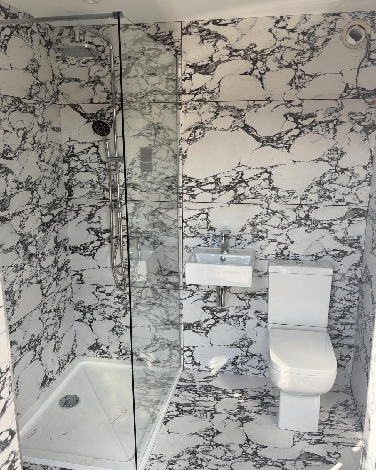 Bathroom installation with marble-patterned walls, a glass shower enclosure, basin and toilet